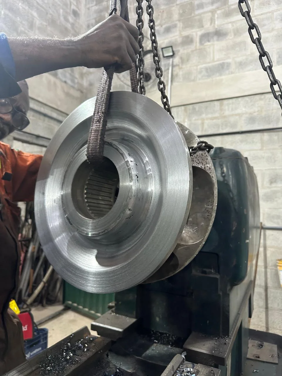Machined component being lifted by sling and chain hoist in the workshop
